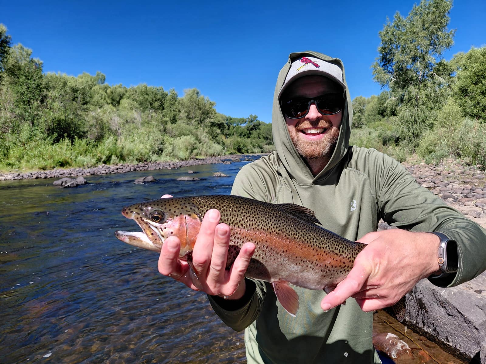 Angler wading a Colorado river holding a rainbow trout