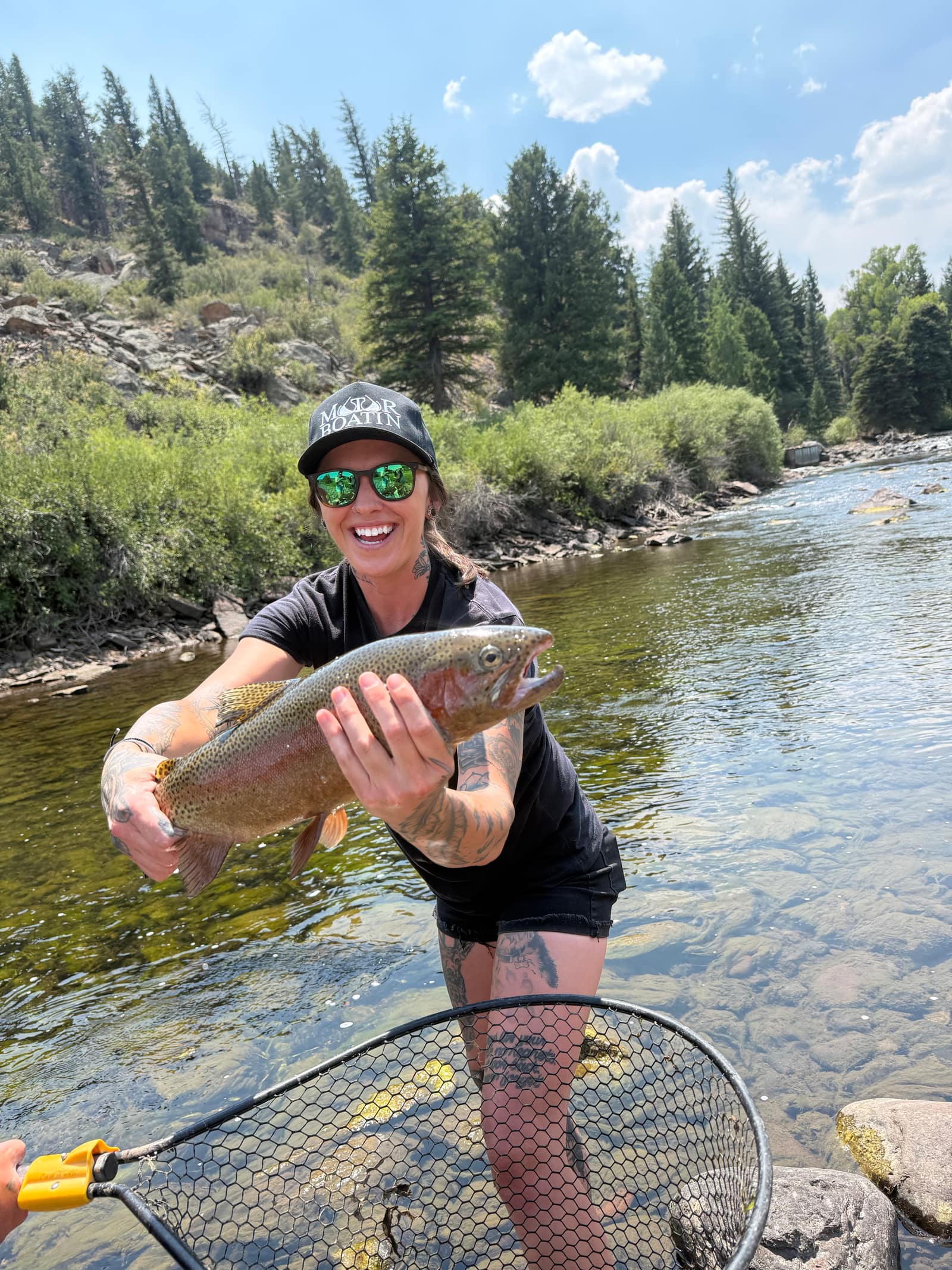Angler holding a trout on a pine-lined mountain river