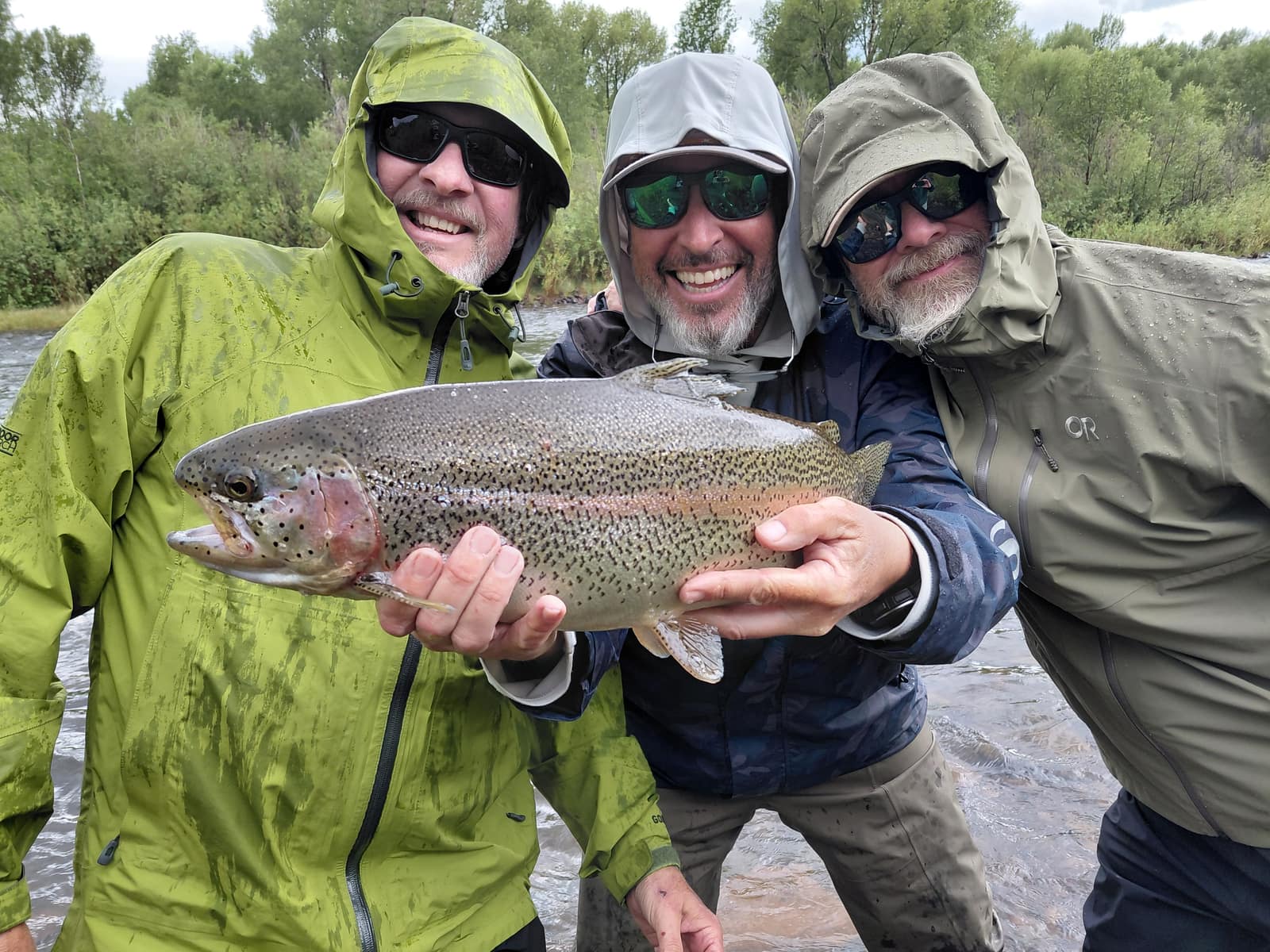Three anglers on a Colorado river holding a rainbow trout together