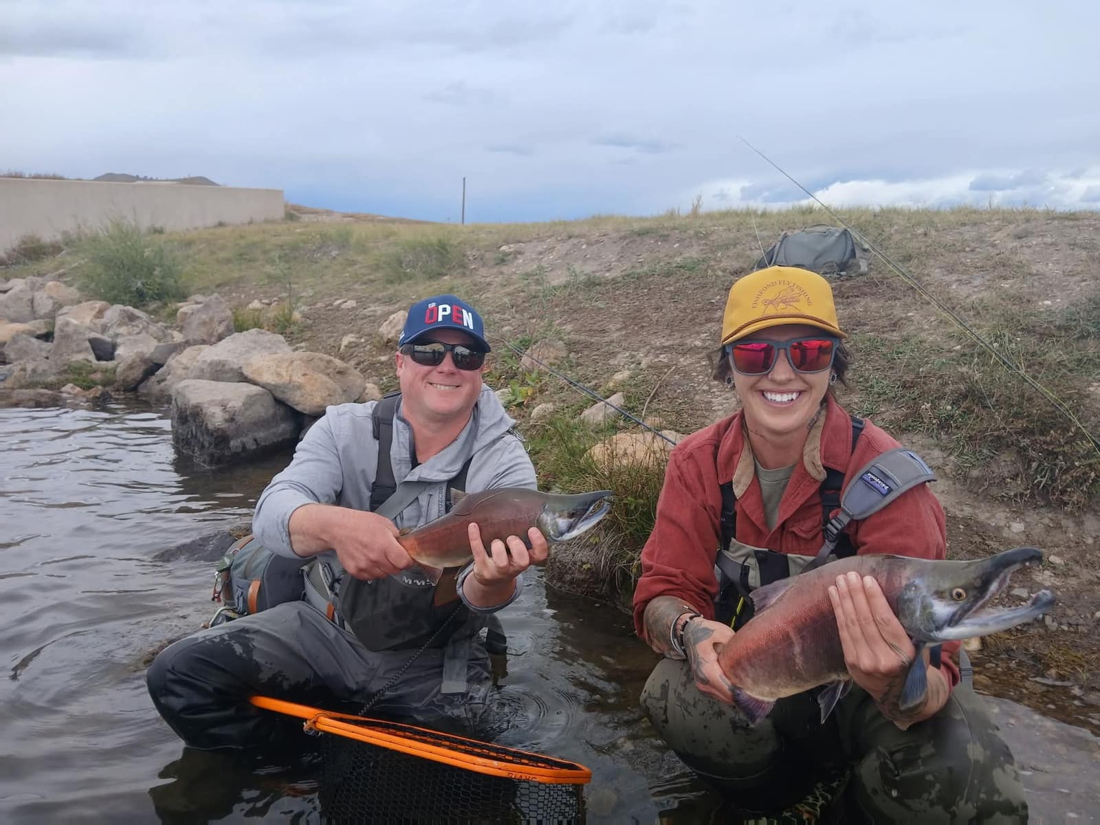Two anglers kneeling in the shallows holding kokanee salmon