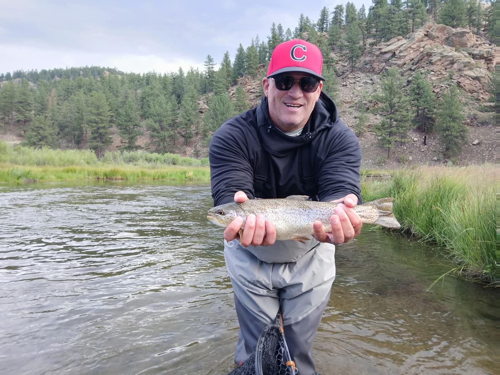 Angler holding a rainbow trout on the South Platte below a pine-covered hillside