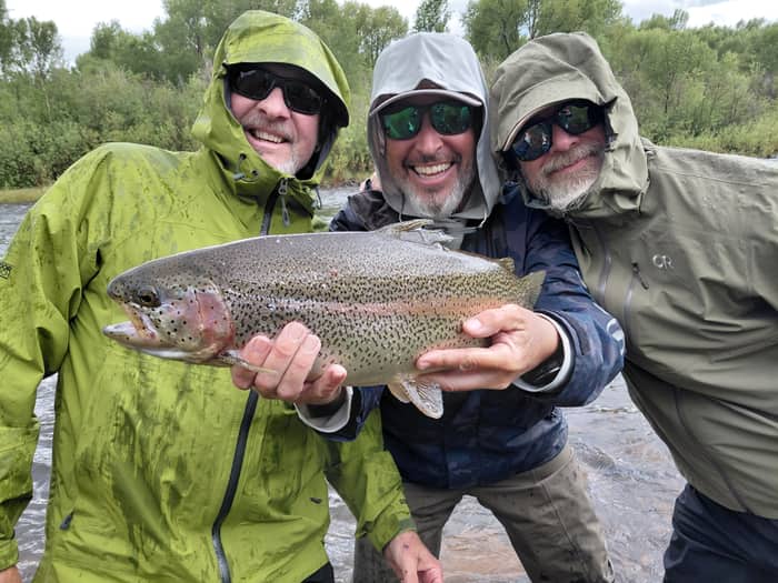 Three anglers holding a rainbow trout together