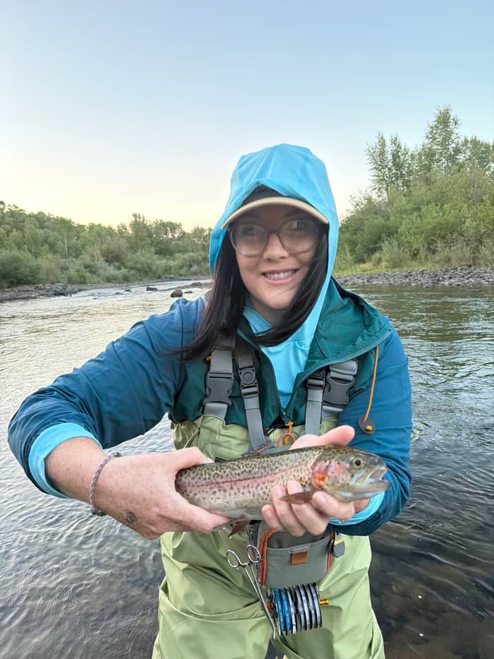 Angler in rain jacket holding a rainbow trout