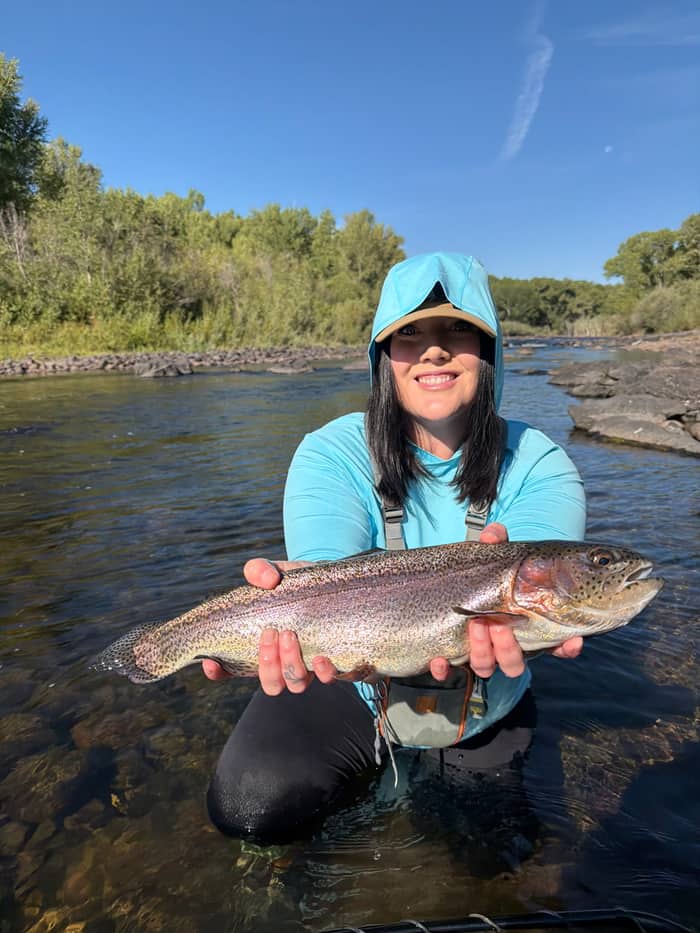 Angler holding a rainbow trout under a clear blue sky