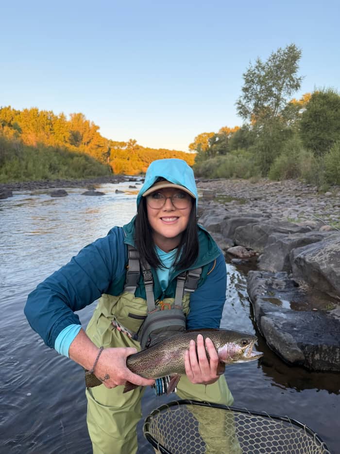 Angler kneeling with a rainbow trout at the water's edge