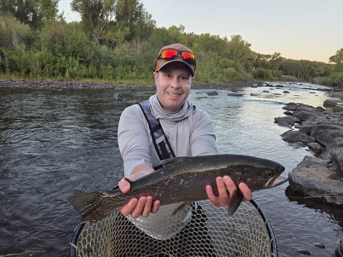 Angler holding a rainbow trout at sunset
