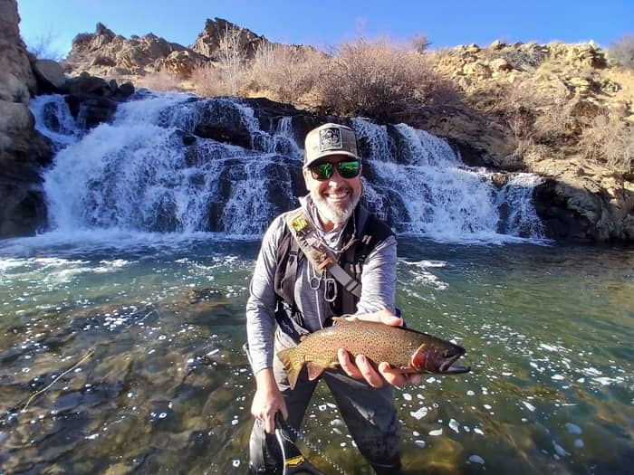 Angler holding a trout below a desert canyon waterfall